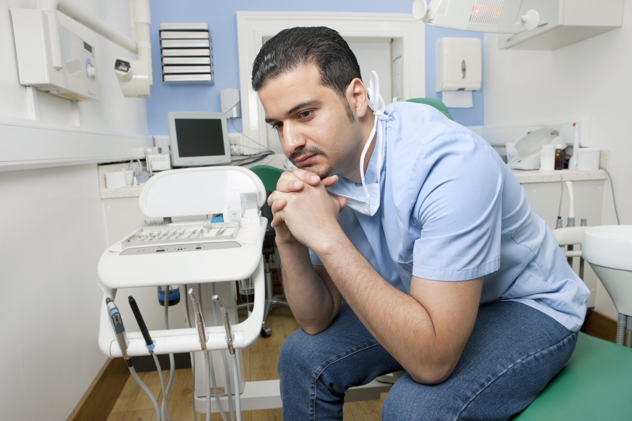 Worried looking dentist sitting on dentist chair in his clinic,, waiting for customers.